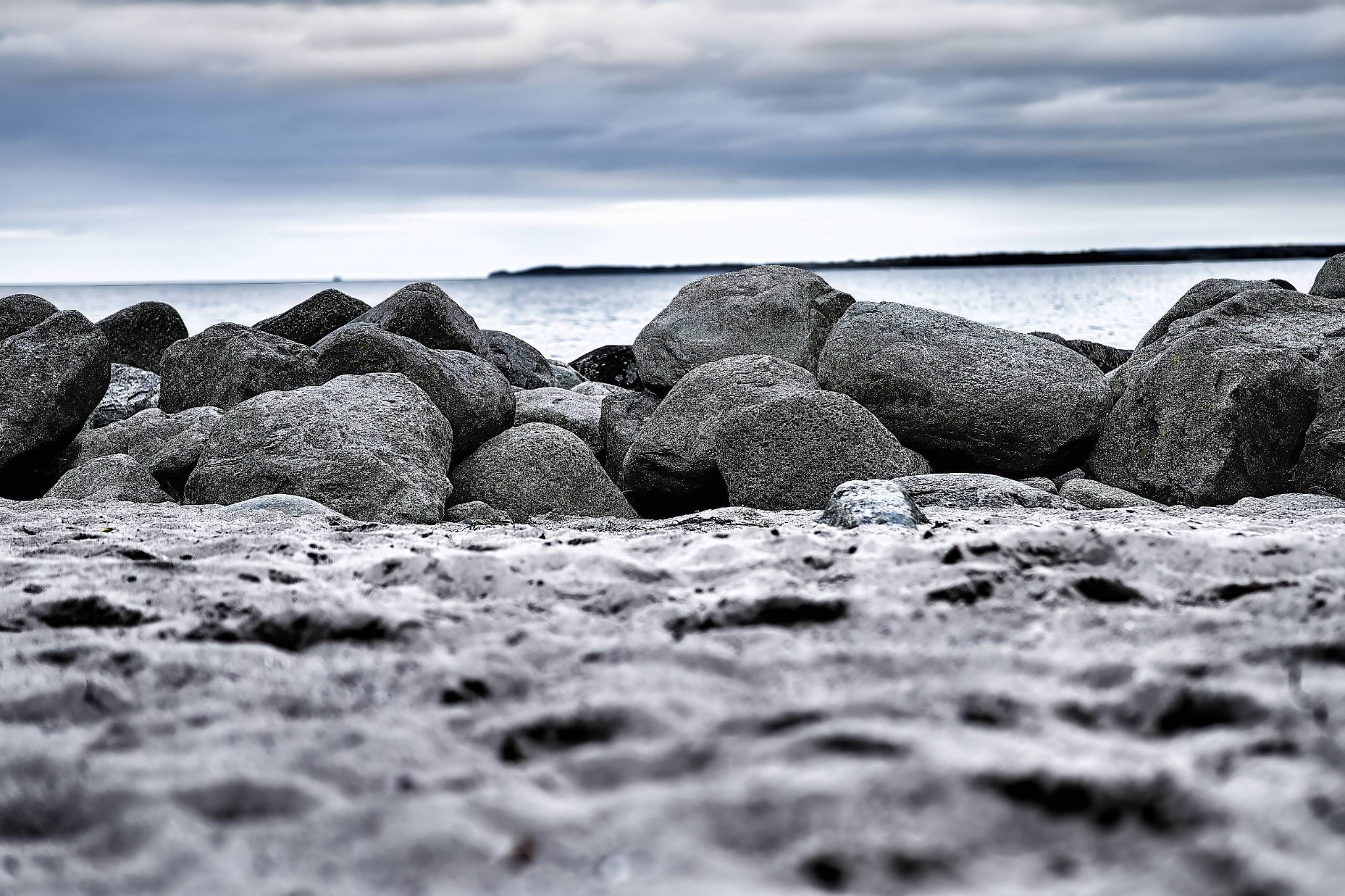 Große graue Felsblöcke liegen an der polnischen Ostseeküste zwischen unscharfem Vordergrund, ruhigem Wasser und tief hängender Wolkendecke.