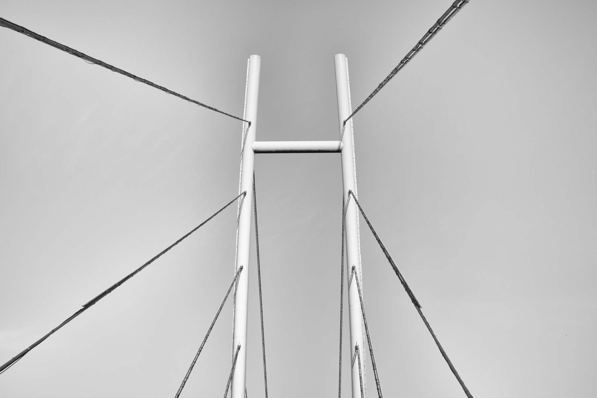 Blick von unten entlang einer Brücke bei Mikołajki: zwei helle Pylone und gespannte Seile laufen nahezu symmetrisch vom Bildzentrum nach außen.