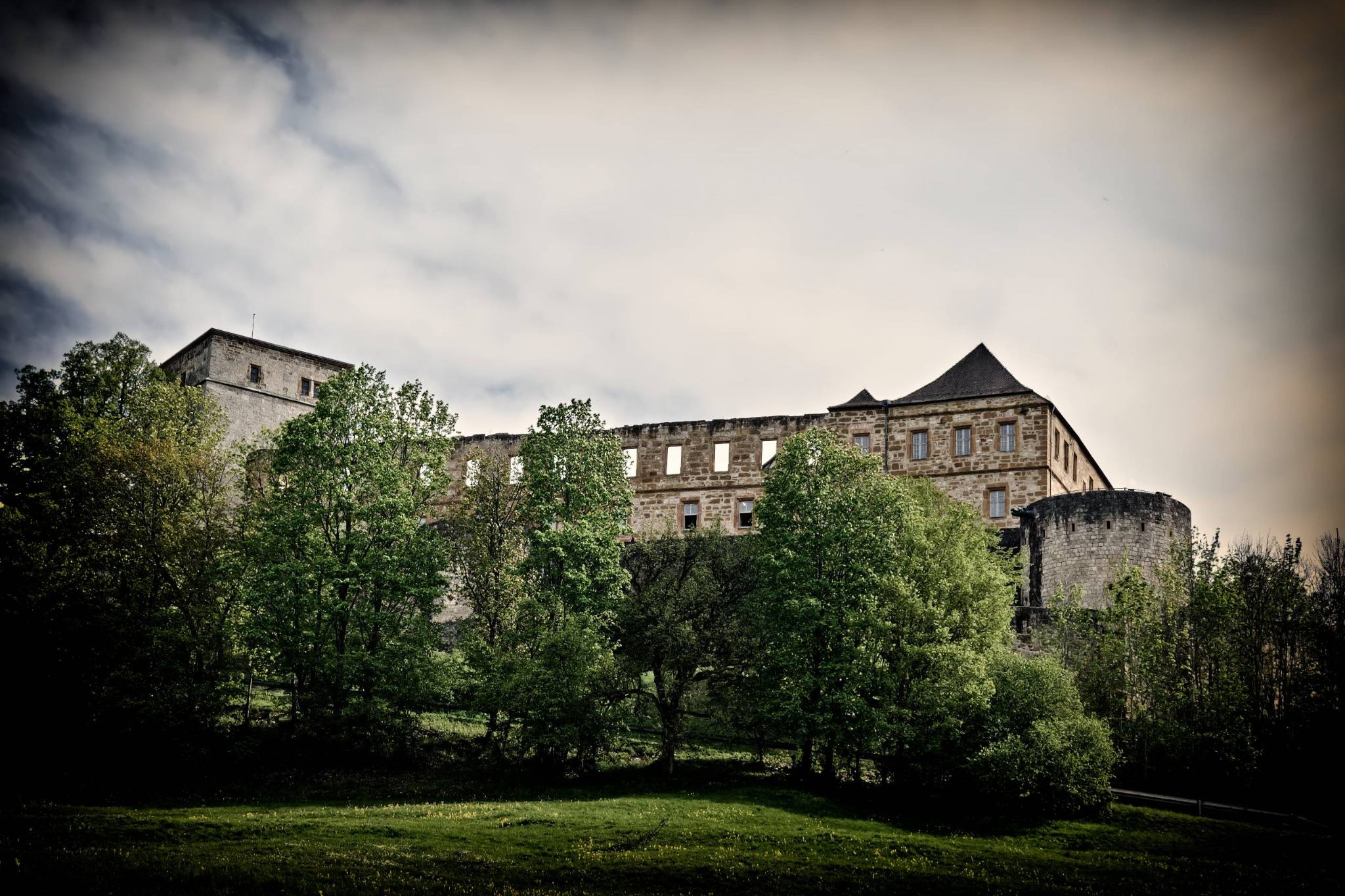 Die historische Giechburg erhebt sich über dichtem Grün unter einem hellen, bewölkten Himmel.